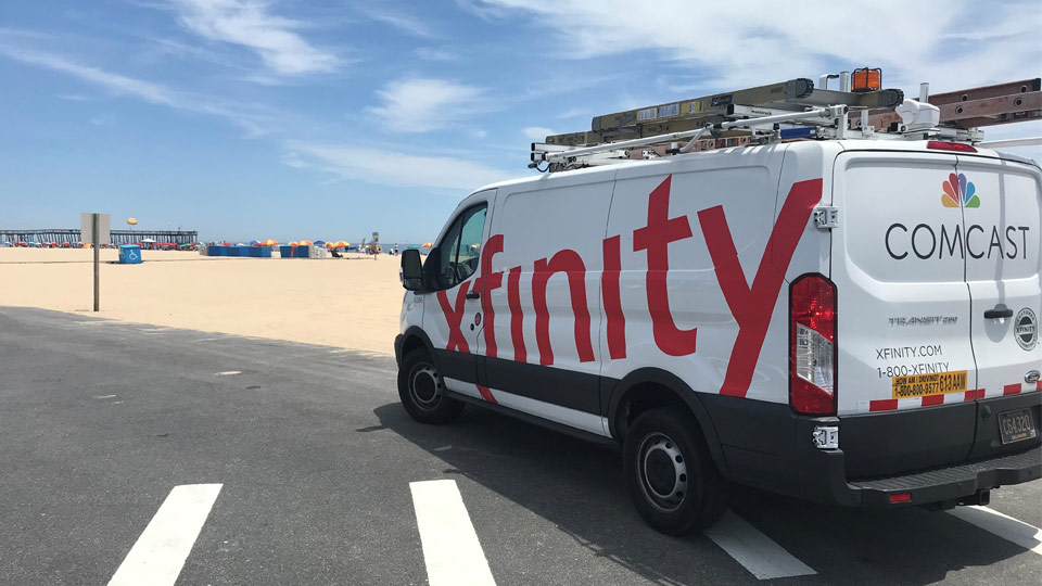 An Xfinity van is parked next to a beach.