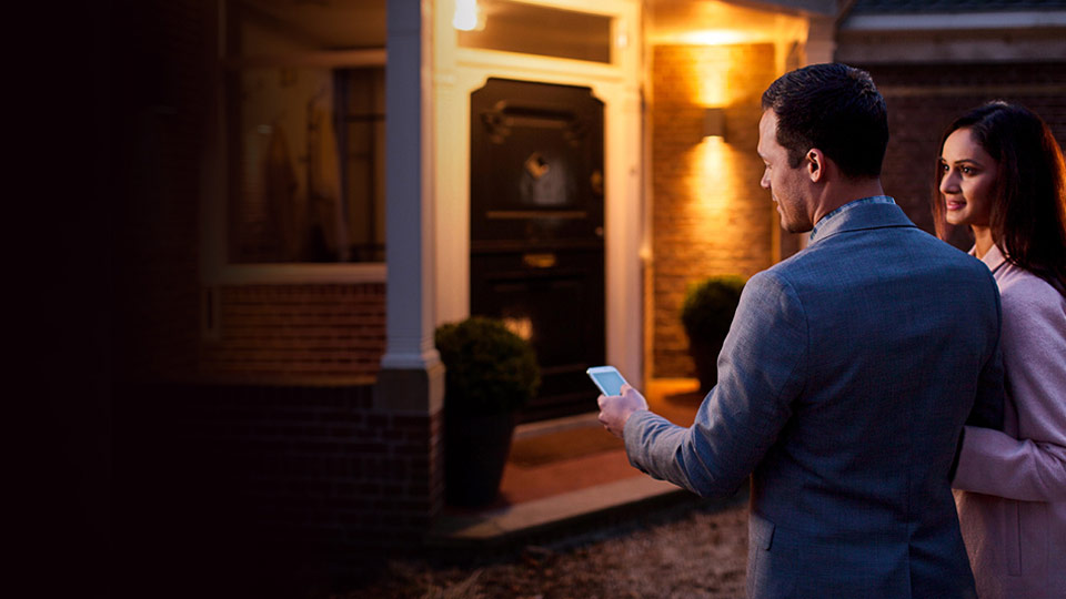 Two people use a mobile phone as they approach the front door of a house.