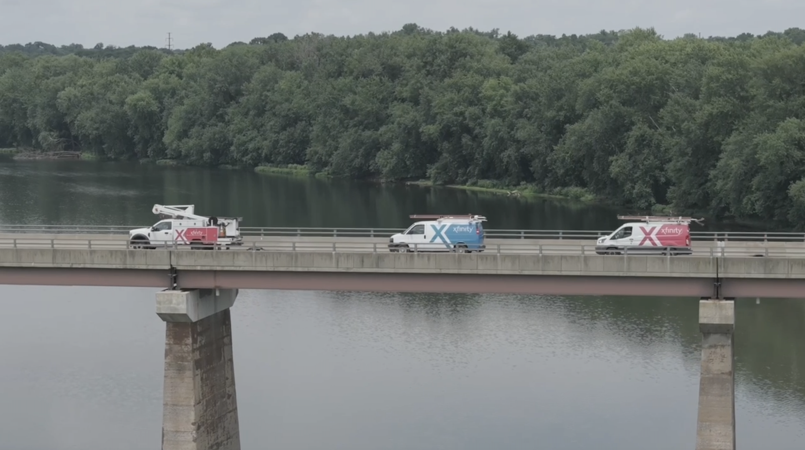 Three Xfinity trucks driving across bridge.